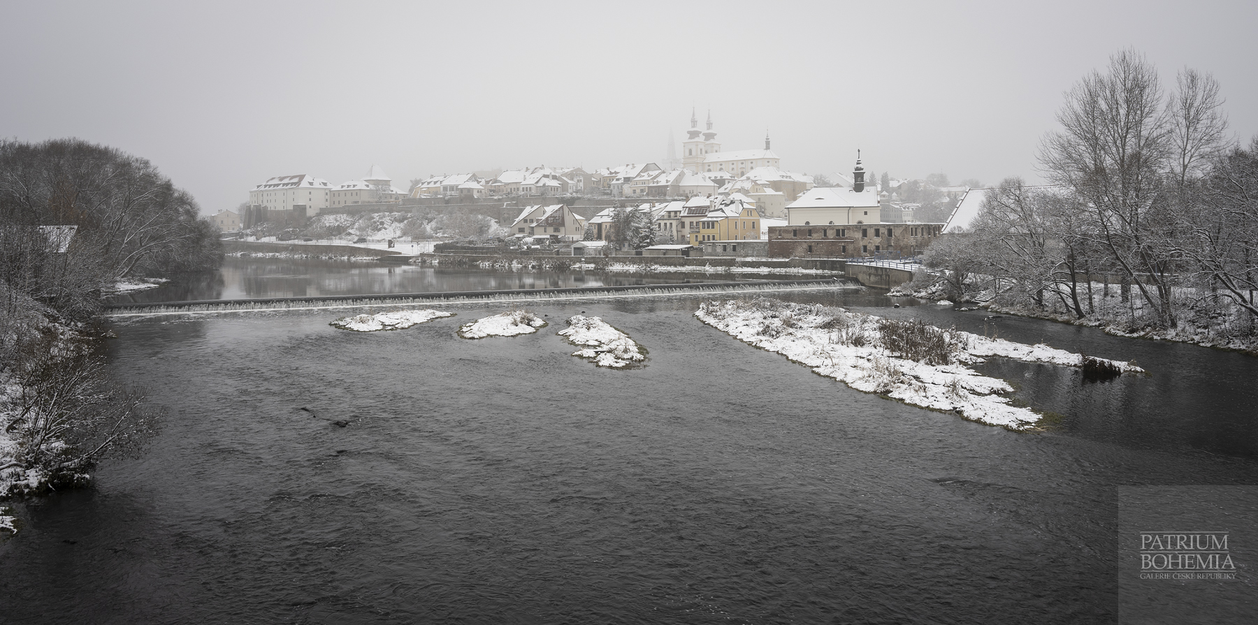 Řeka Ohře a část zasněženého města Kadaň v zimě, vlevo hrad Kadaň.