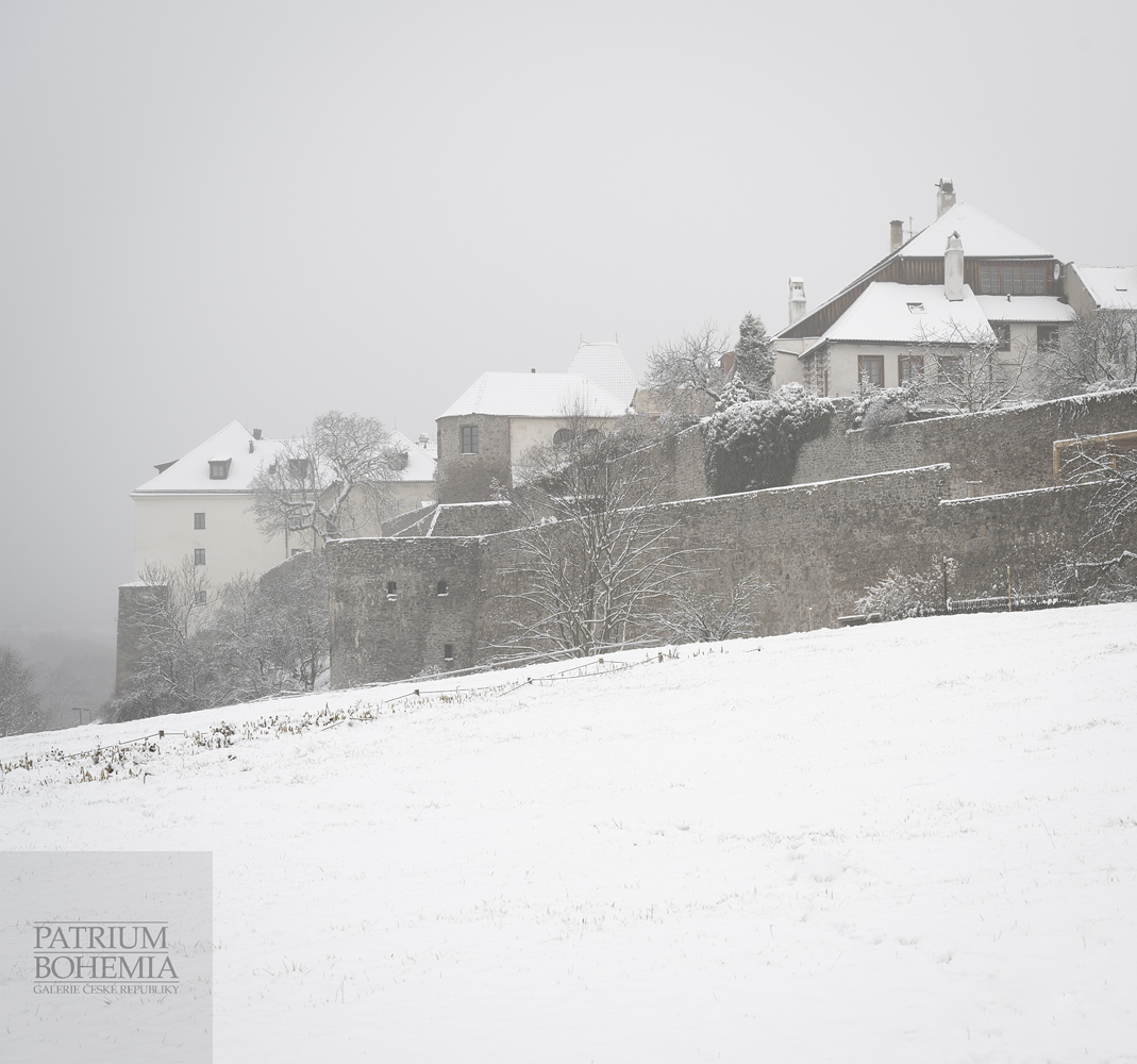 Pohled z Žatecké ulice na mohutné, zasněžené městské hradby. Vlevo hrad Kadaň.