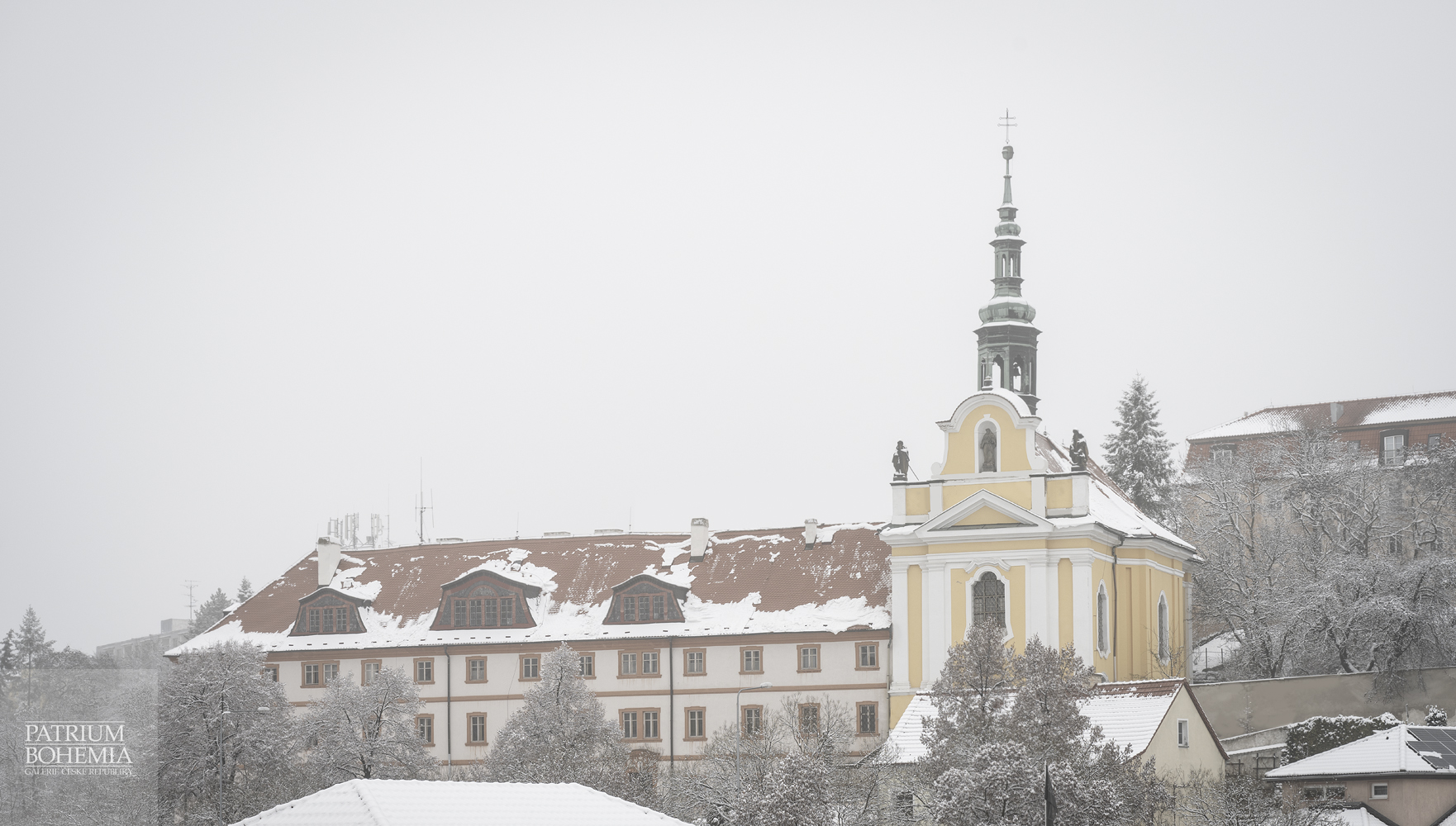 Dvě významné kadaňské barokní památky, zasněžené v zimě – vlevo alžbětinský klášter, vpravo kostel sv. Rodiny a sv. Alžběty. Rokelská ulice.